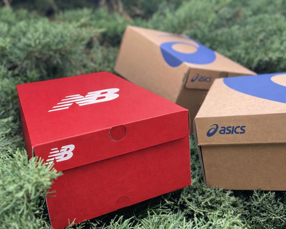 Cajas de las mejores zapatillas de trail running en este 2026, posadas en un seto.